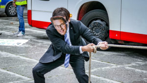Mensch im Anzug mit Andi Scheuer Maske zieht an einem Tauseil